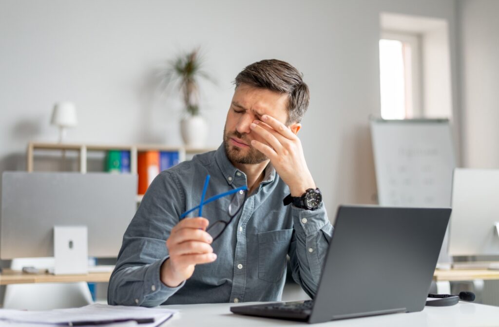 Young adult man rubbing his dry eyes while working at a laptop.