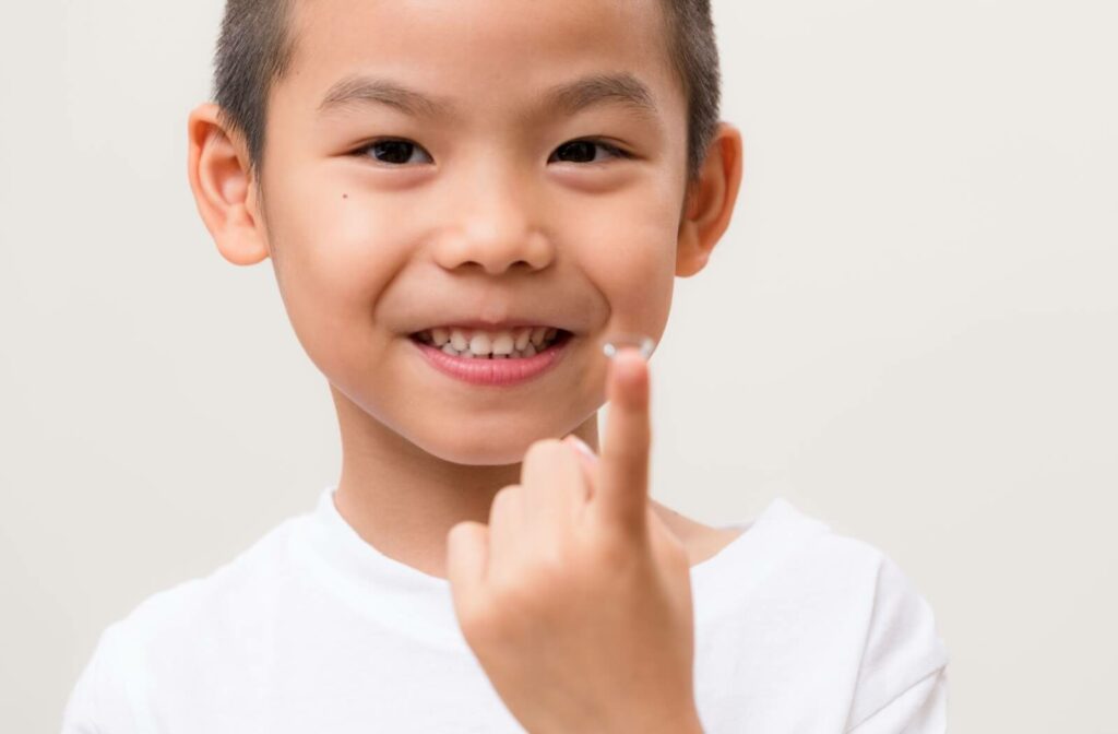 an enthusiastic and smiley child hold a contact lens in his index finger.